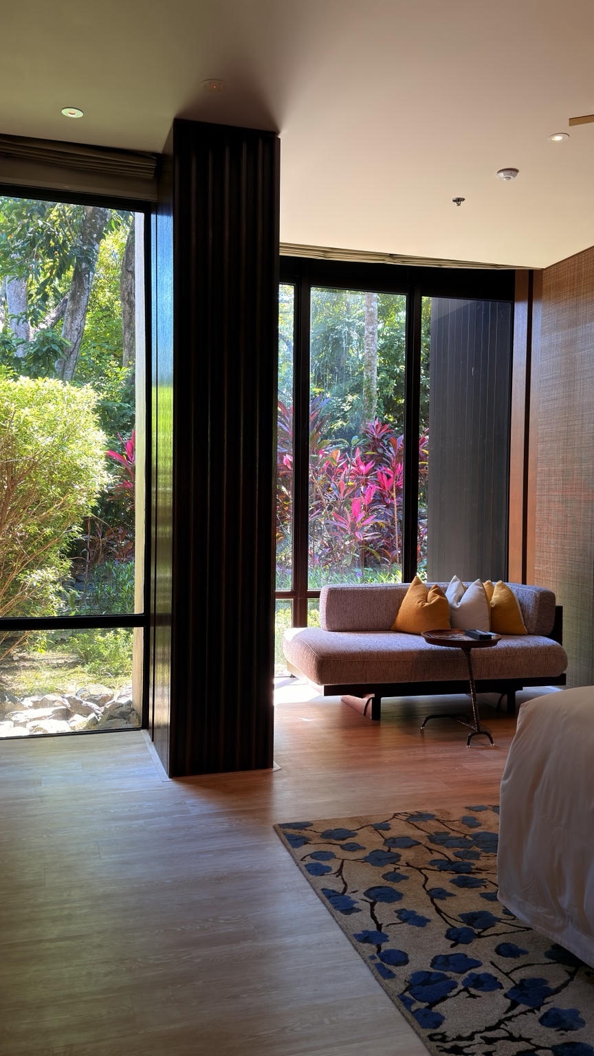 A hotel sitting area with a sofa beside a window overlooking greenery